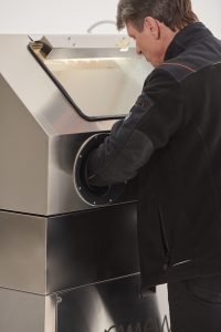 Pracownik warsztatowy przy myjce wysokociśnieniowej MEWA z zamkniętą komorą